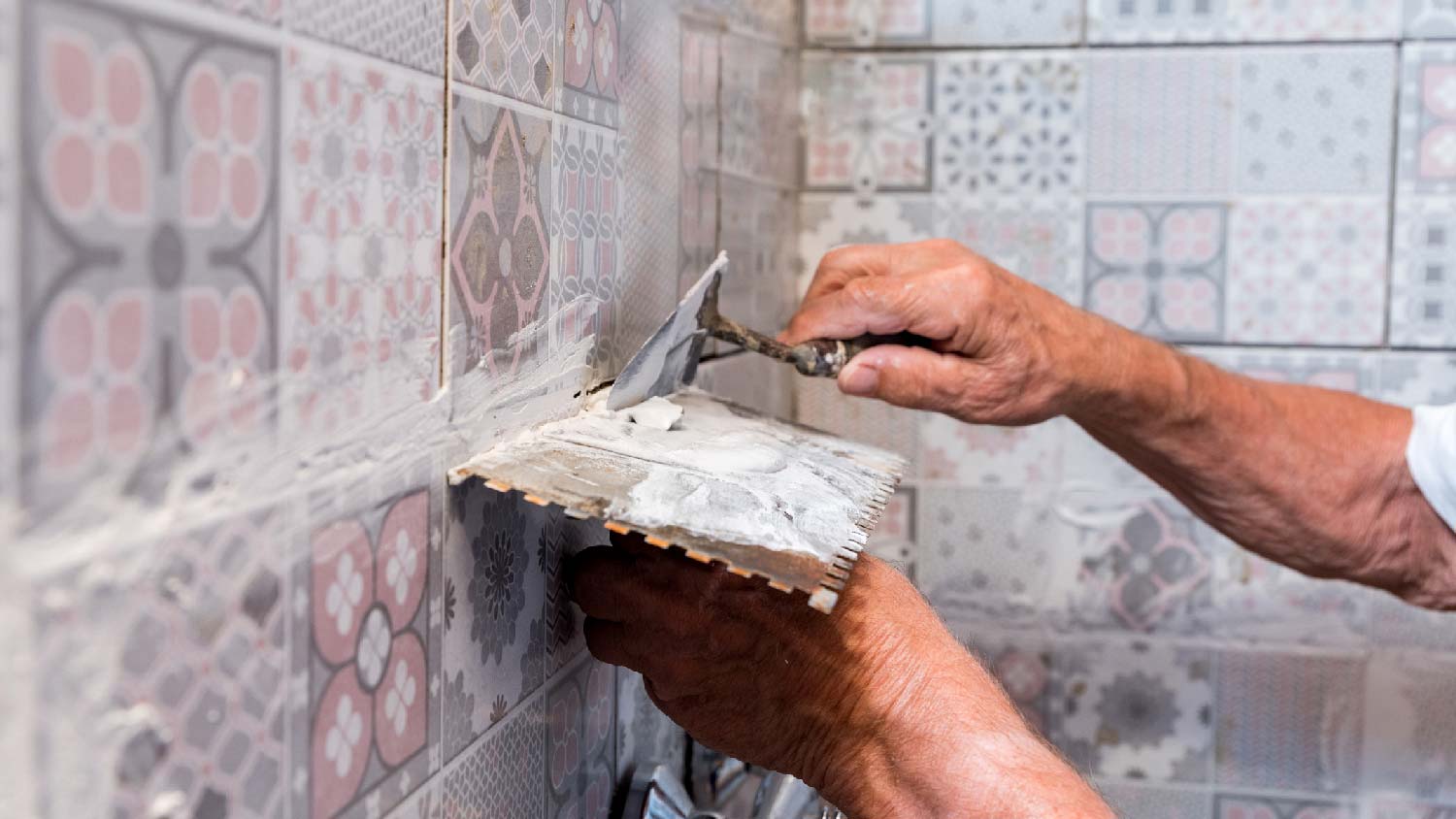 A senior man grouting tiles on a wall